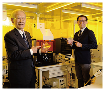 検出用のマイクロチップを手にする松本紘理事長(写真左)と渡邉力也主任研究員の写真