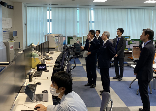 中央制御室で田中 副センター長から説明を受けられる盛山 大臣の写真