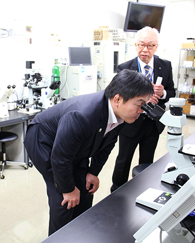 濱田博司センター長と顕微鏡を覗き込む馳浩(はせ ひろし)文部科学大臣