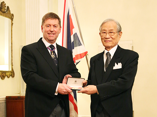 叙勲式の写真：ポール・マデン駐日英国大使より勲章を受け取る松本紘理事長