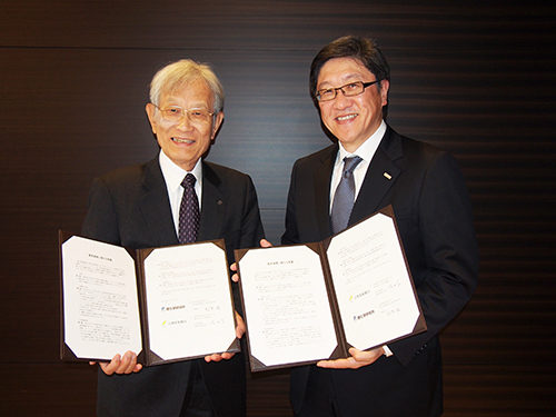 覚書を手にする成田学副頭取（右）と松本紘理事長（左）の写真