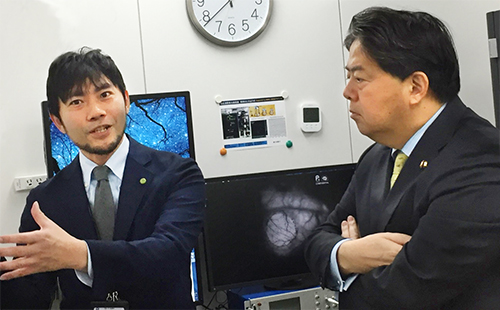 村山チームリーダーから説明を受ける林大臣(右)の写真