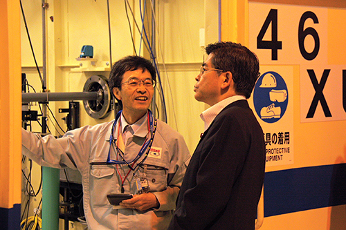 JASRIの廣沢一郎産業利用推進室長から説明を受ける石井大臣（SPring-8 共用ビームライン46XUにて）の写真