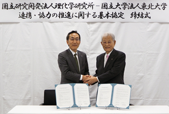 「基本協定締結後に握手する松本理事長（右）と大野総長（左）の写真
