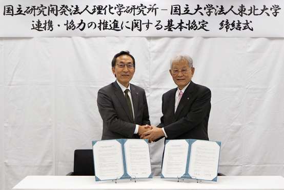 「基本協定締結後に握手する松本理事長(右)と大野総長(左)の写真
