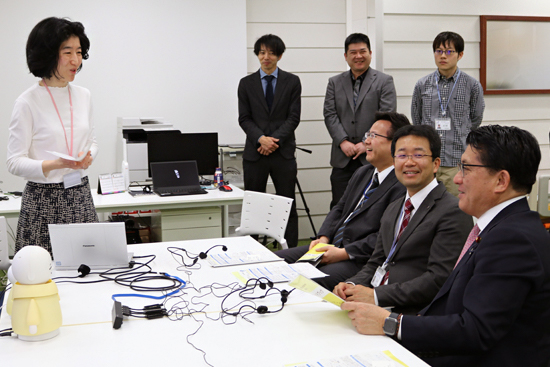 平井大臣（右から一人目）との会話が弾む杉山センター長（右から二人目）と大武チームリーダー（左）の写真