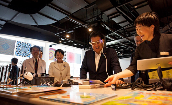 髙橋プロジェクトリーダーの案内によりビジョンパークの展示品を体験する平井大臣の写真
