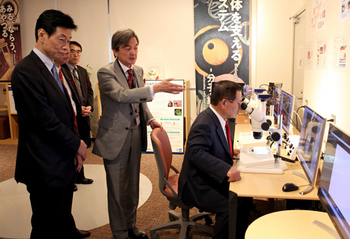 辻チームリーダーから説明を受ける西村大臣と竹本大臣の写真