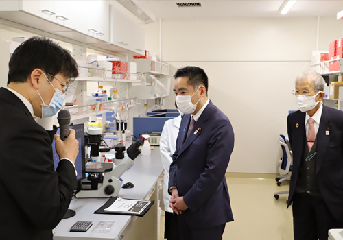 井上チームリーダーから説明を受ける井上大臣(右は松本理事長)の写真